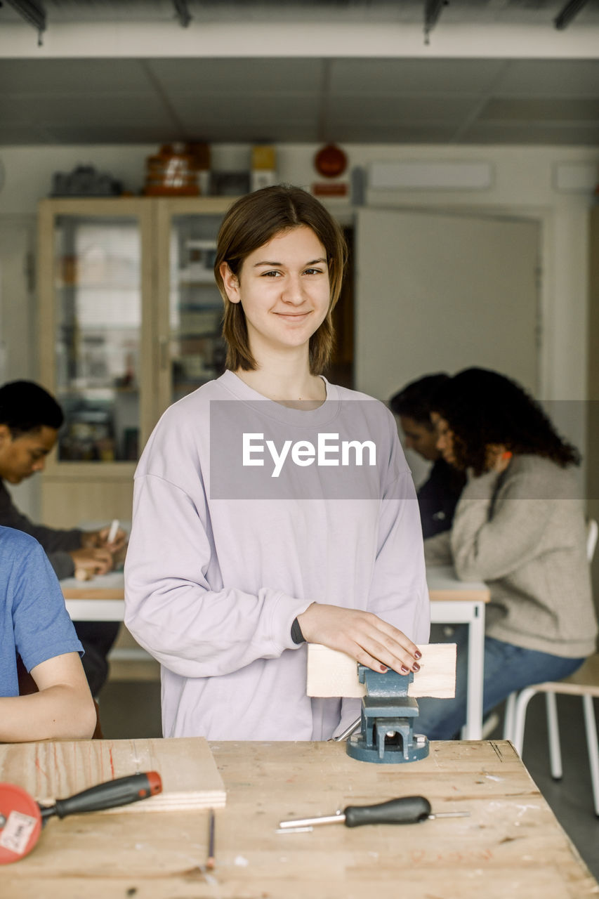 Portrait of smiling female teenage student fixing wood on clamp during carpentry class