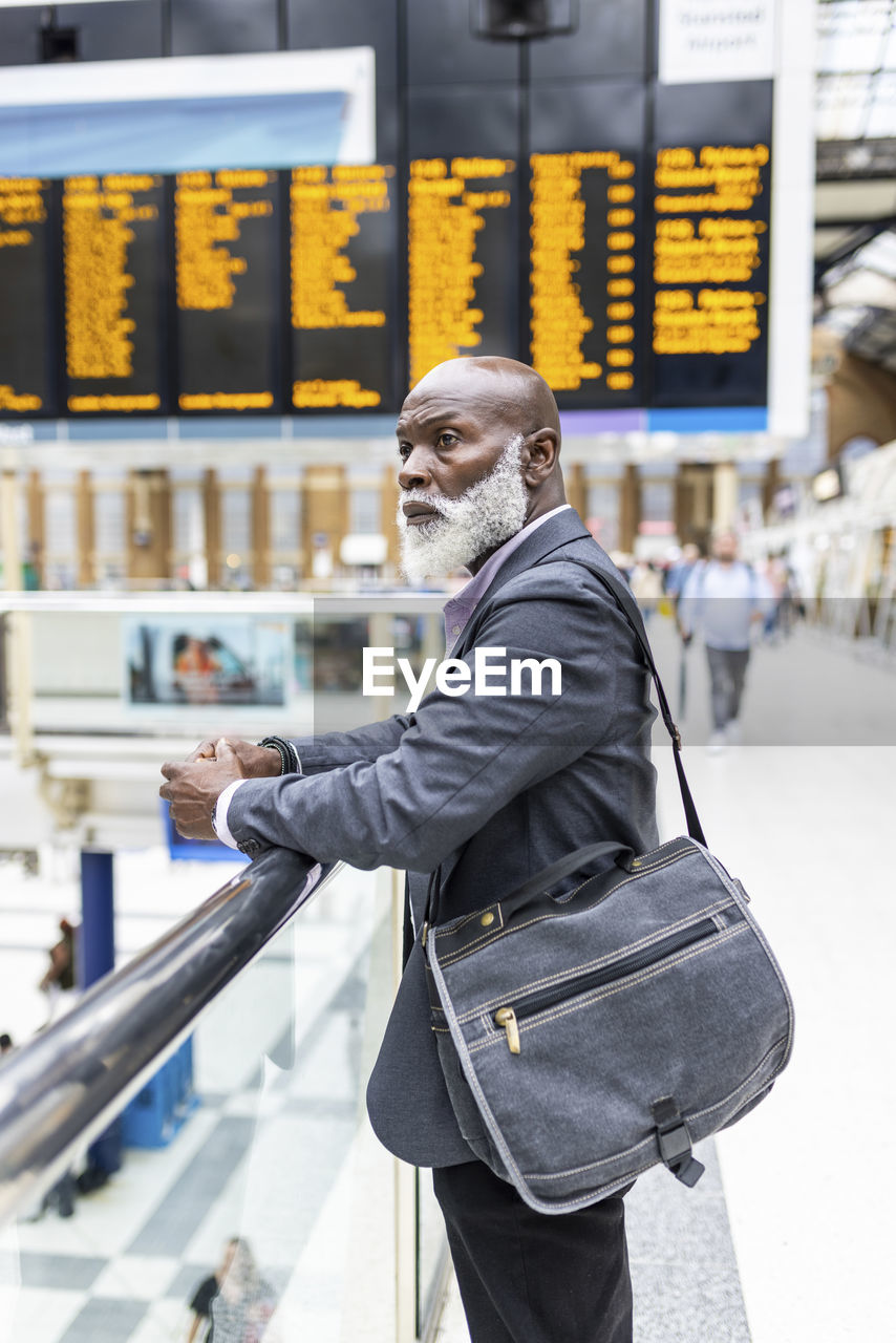 Contemplative businessman with laptop bag leaning on railing at station