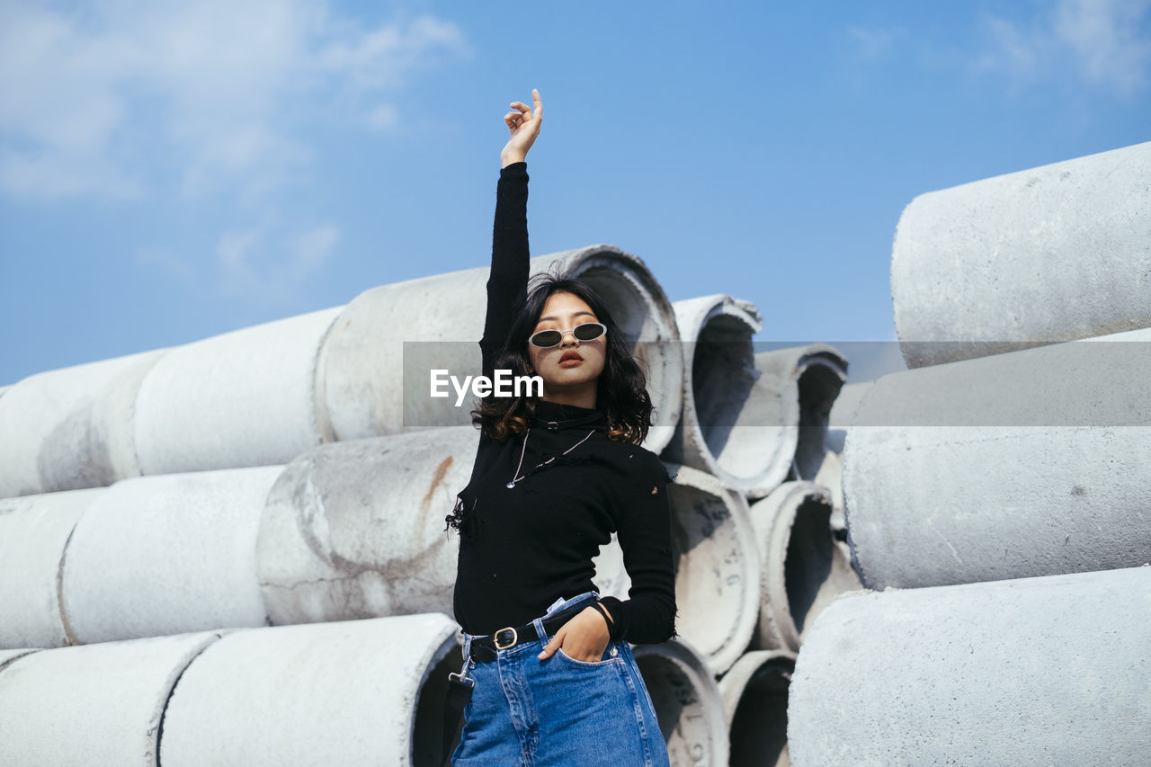 LOW ANGLE VIEW OF YOUNG WOMAN STANDING AGAINST THE SKY