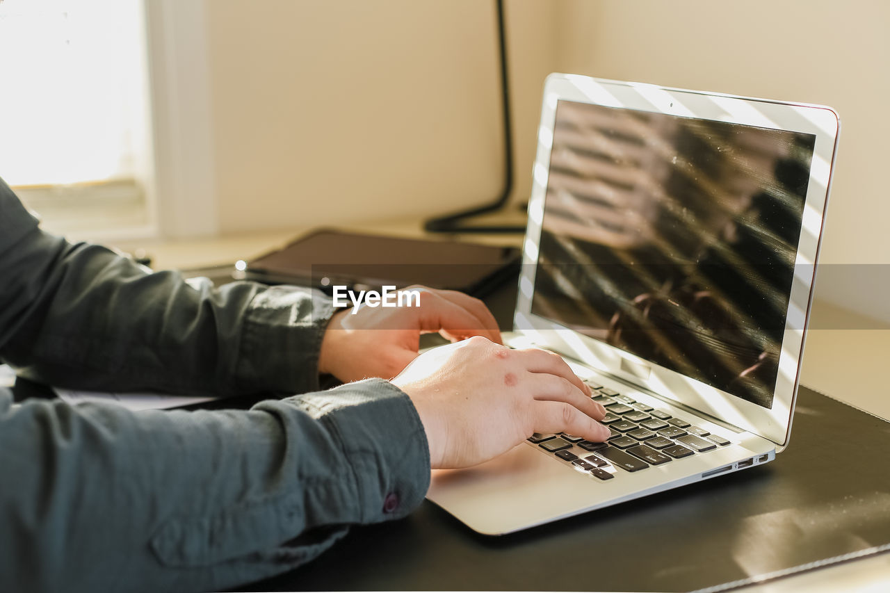 Cropped hands of man using laptop at home