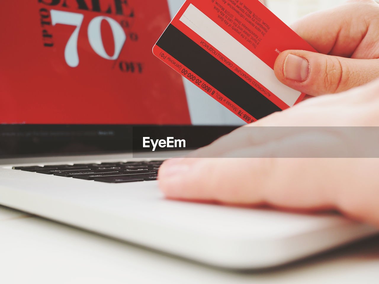 Man holds a credit card in his arm on red sale banner on background