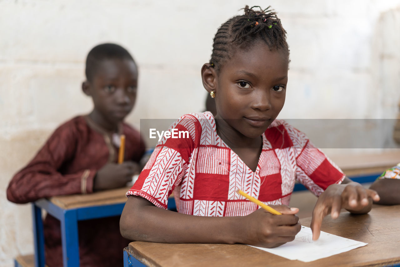 Portrait of girl writing at table in classroom