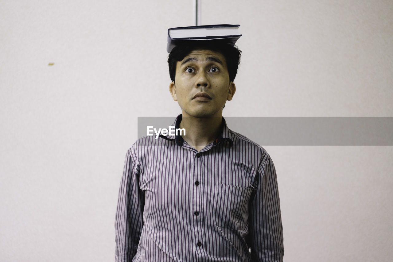 Mid adult man balancing book on head while standing against wall