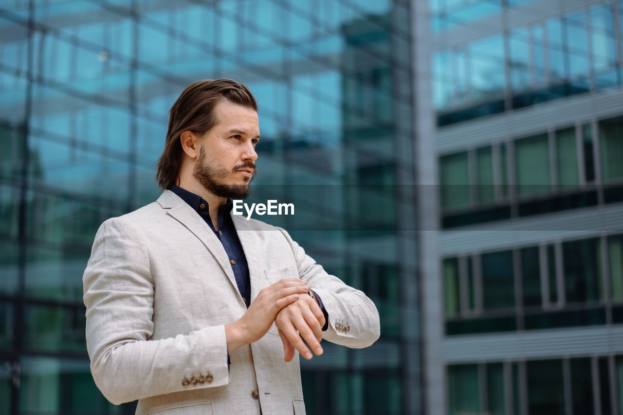 Professional businessman in suit looking at camera while standing on street with mobile phone. app