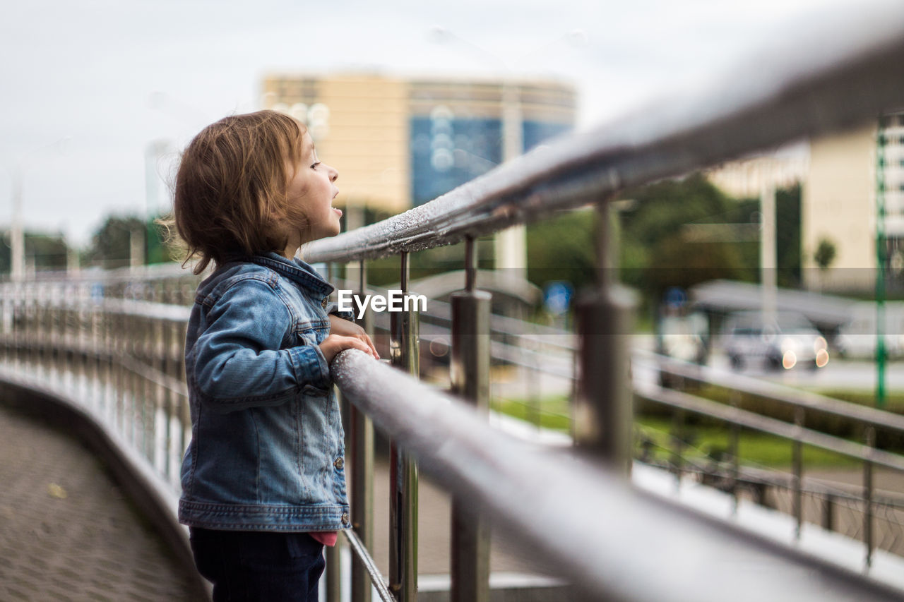 Side view of girl standing on footbridge against sky