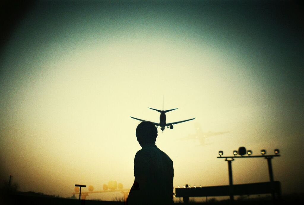 Silhouette man looking at airplane flying in sky