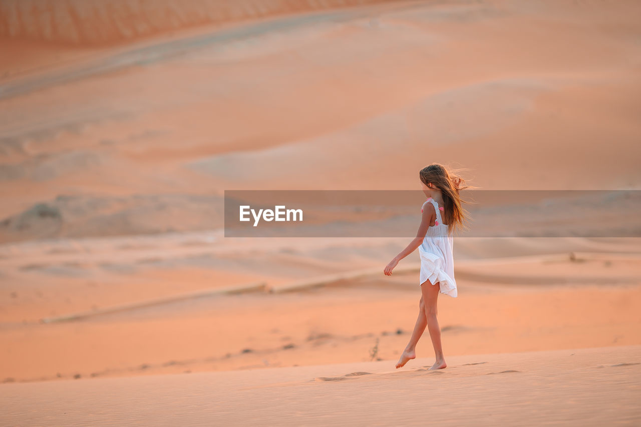 FULL LENGTH OF WOMAN STANDING ON SAND AT BEACH AGAINST SKY