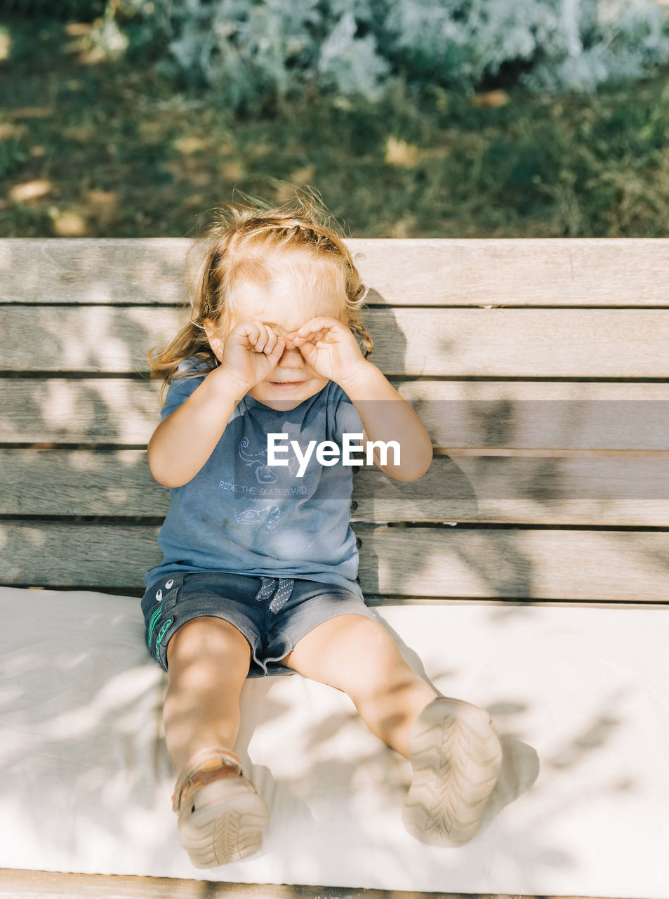 CUTE GIRL SITTING ON BENCH AGAINST BLURRED BACKGROUND