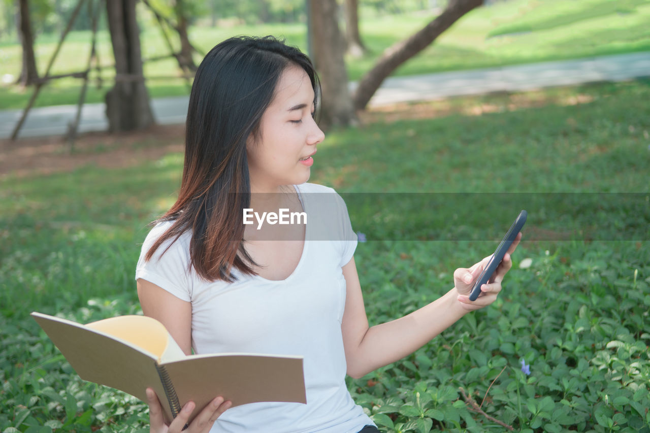 BEAUTIFUL YOUNG WOMAN USING SMART PHONE ON FIELD