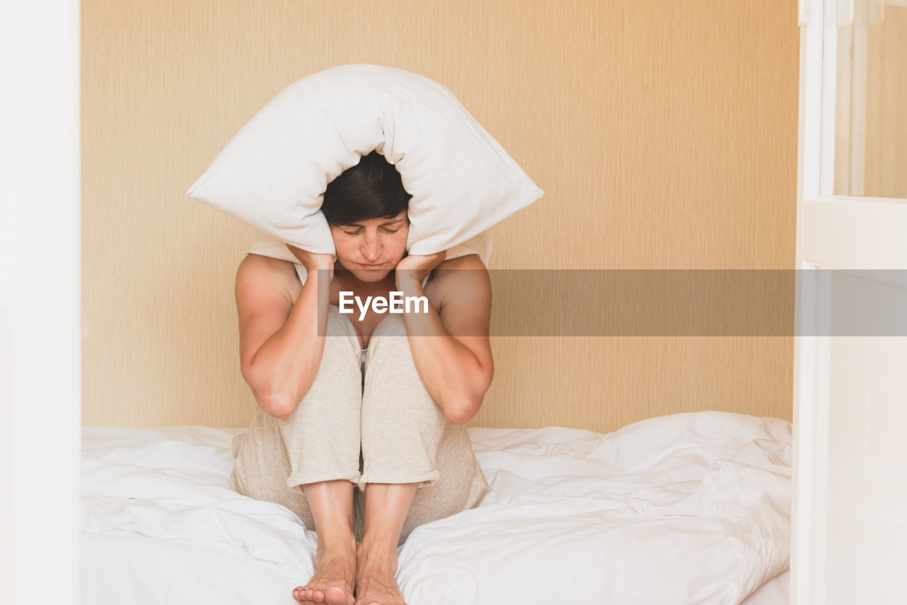 full length of young woman sitting on bed at home