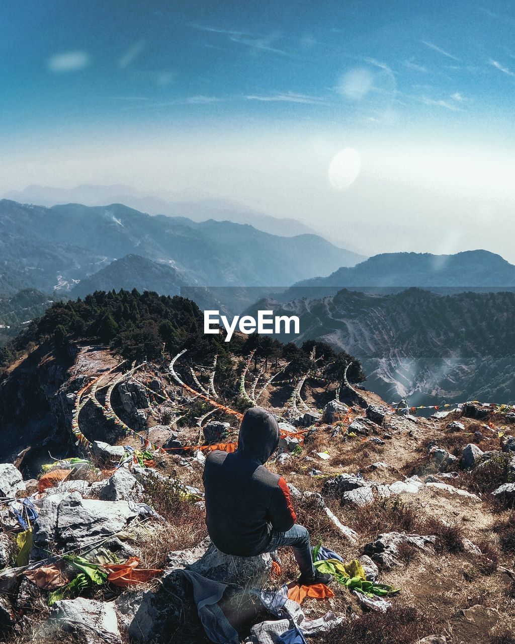 Rear view of man sitting on rock against mountains