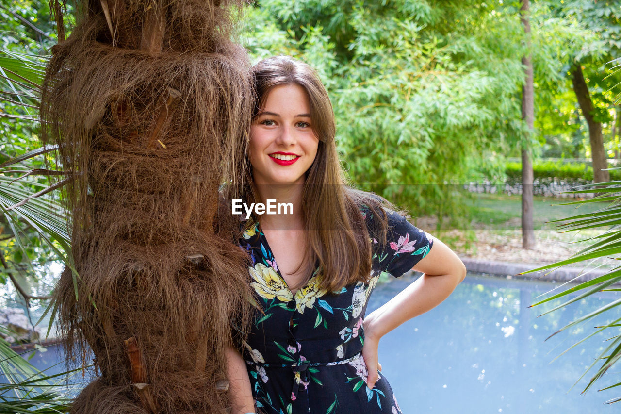 Portrait of smiling young woman by tree trunk