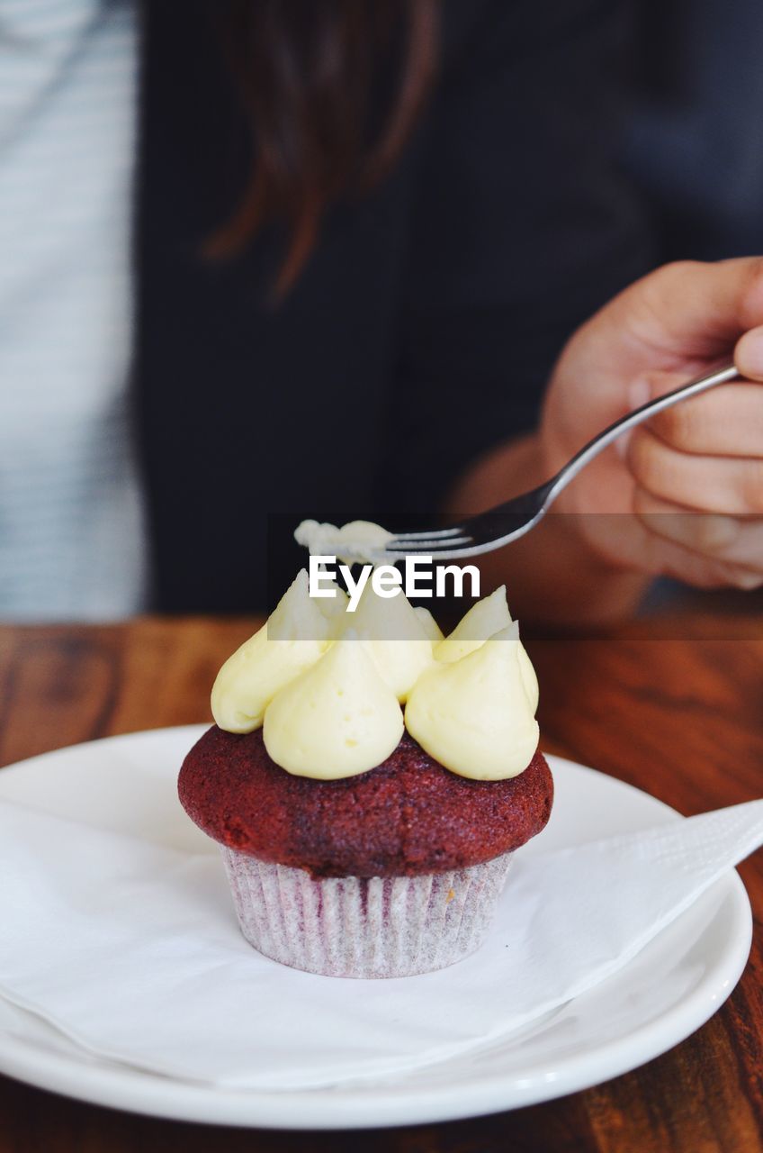 Cropped shot of a persons hand holding a fork tasting a red velvet cupcake 