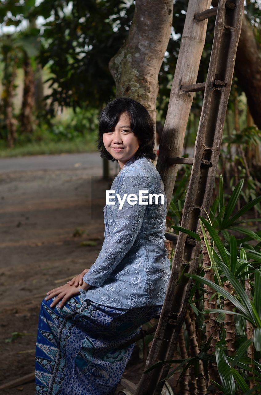 Portrait of smiling young woman sitting on ladder outdoors