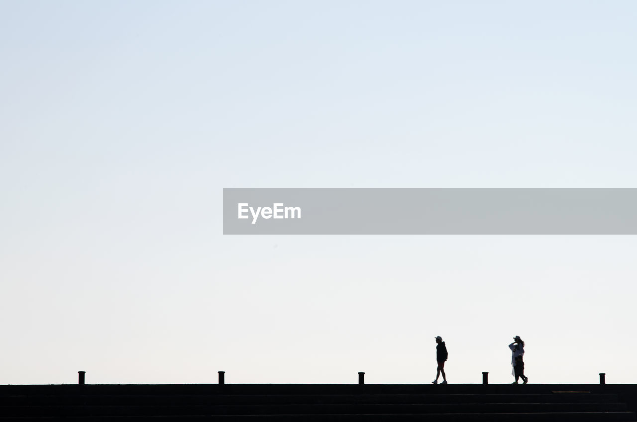 Silhouette people walking on bridge against clear sky