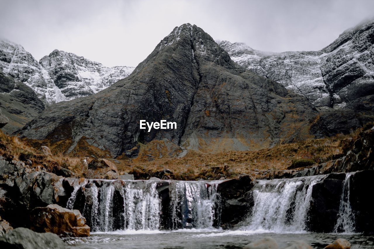 SCENIC VIEW OF WATERFALL AGAINST MOUNTAIN RANGE