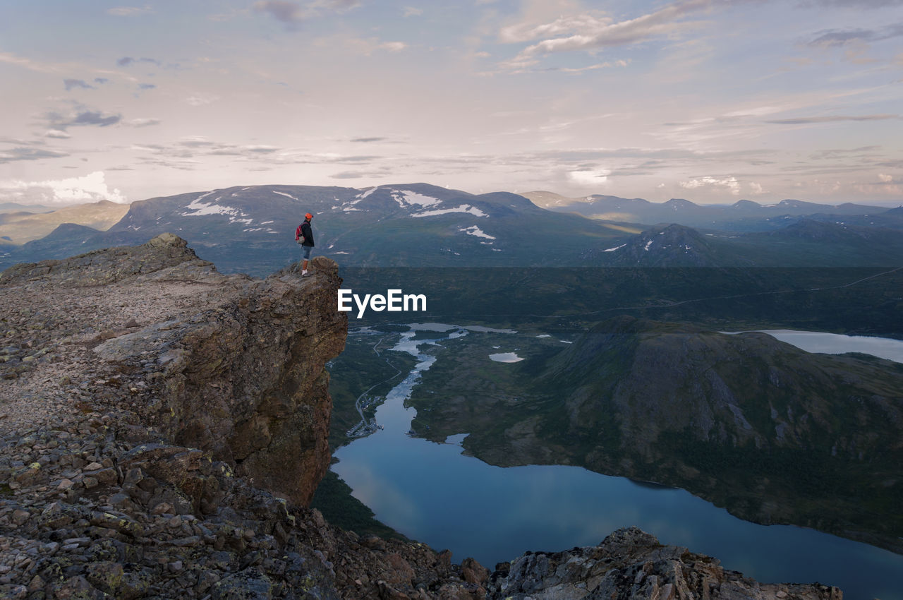 Distant view of man standing on cliff against mountains