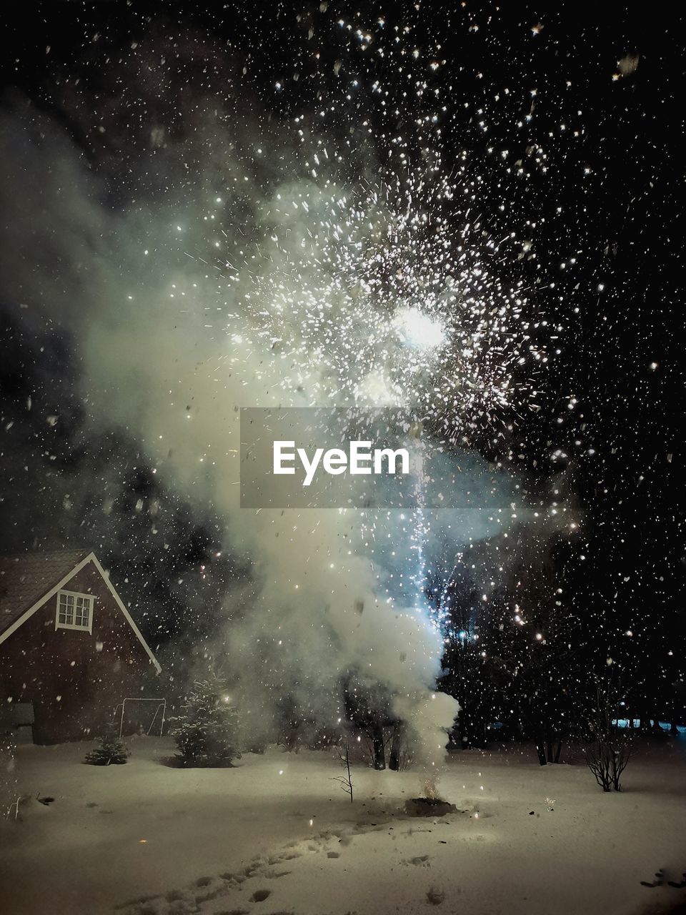 Fireworks explosion with sparks and smoke against sky at night during winter