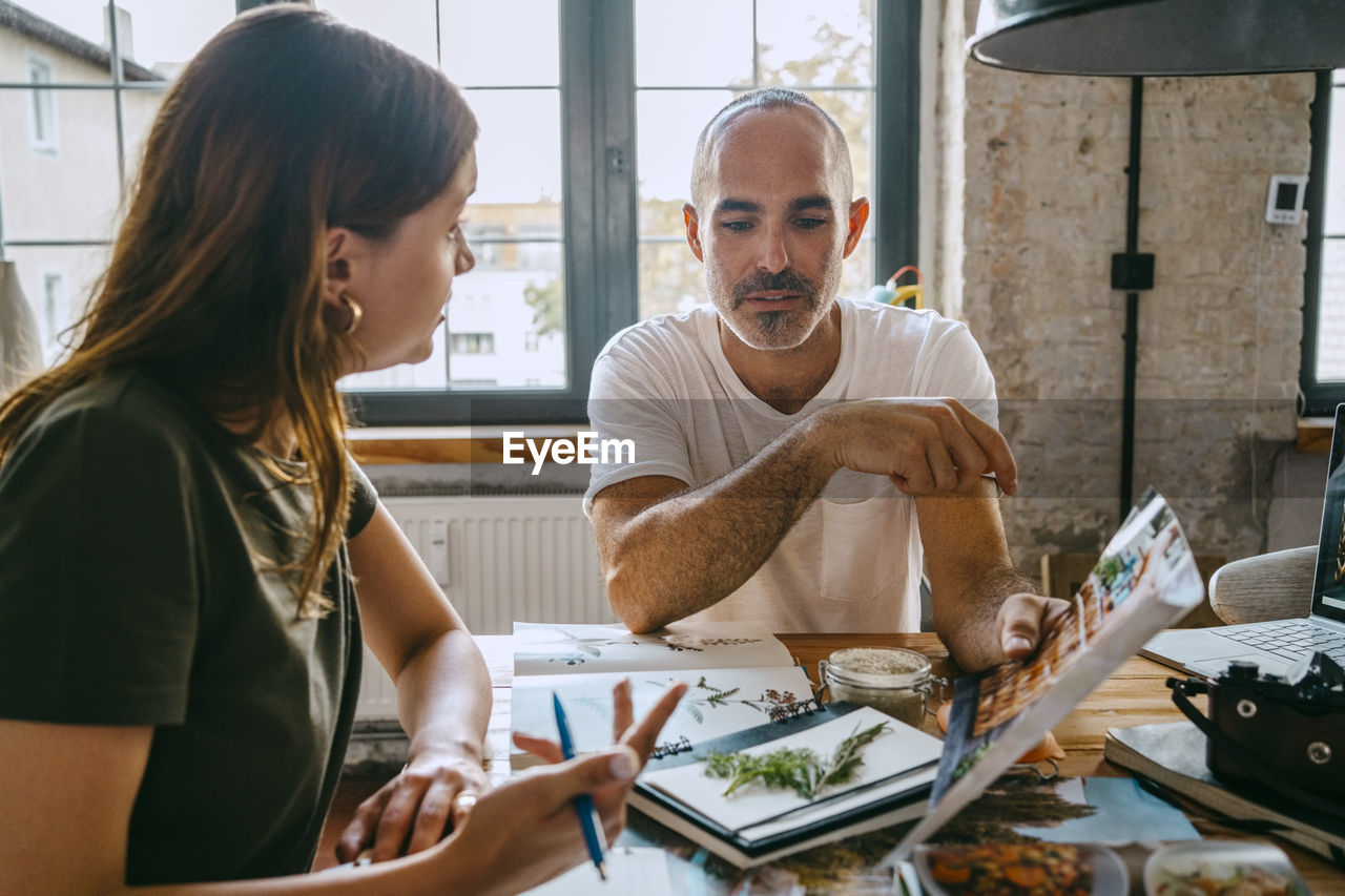 Male entrepreneur holding photograph while explaining to female colleague in studio