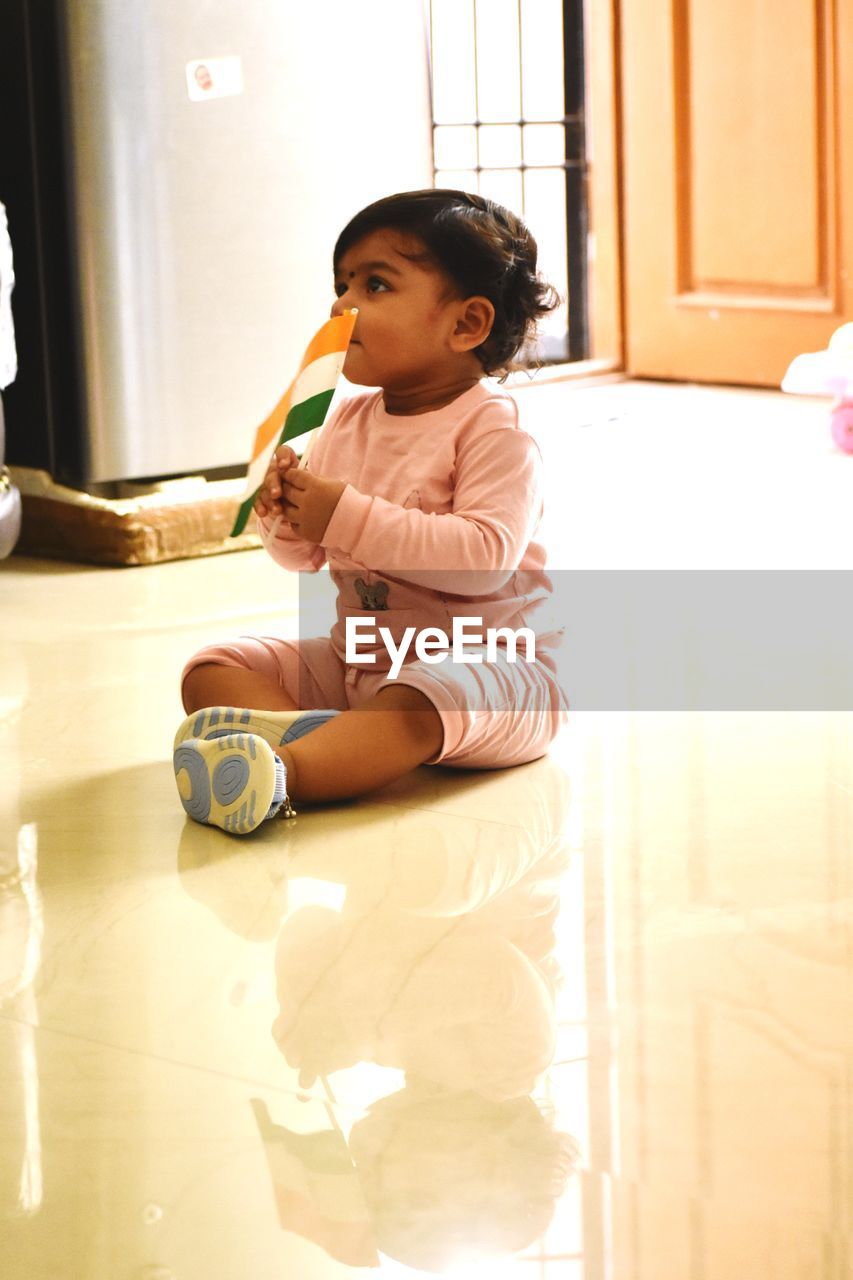 Girl holding indian flag while sitting on floor at home