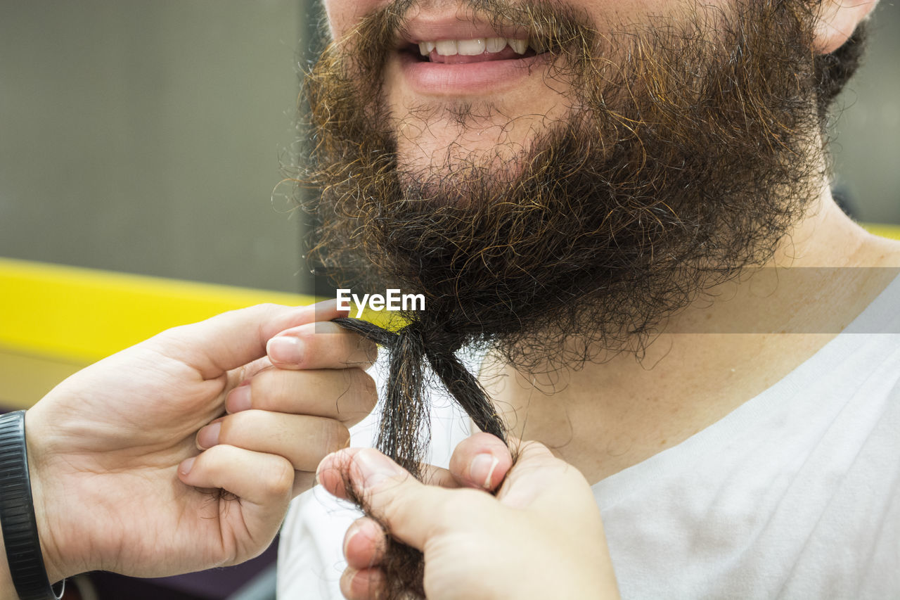 Cropped hands of person tying beard of man