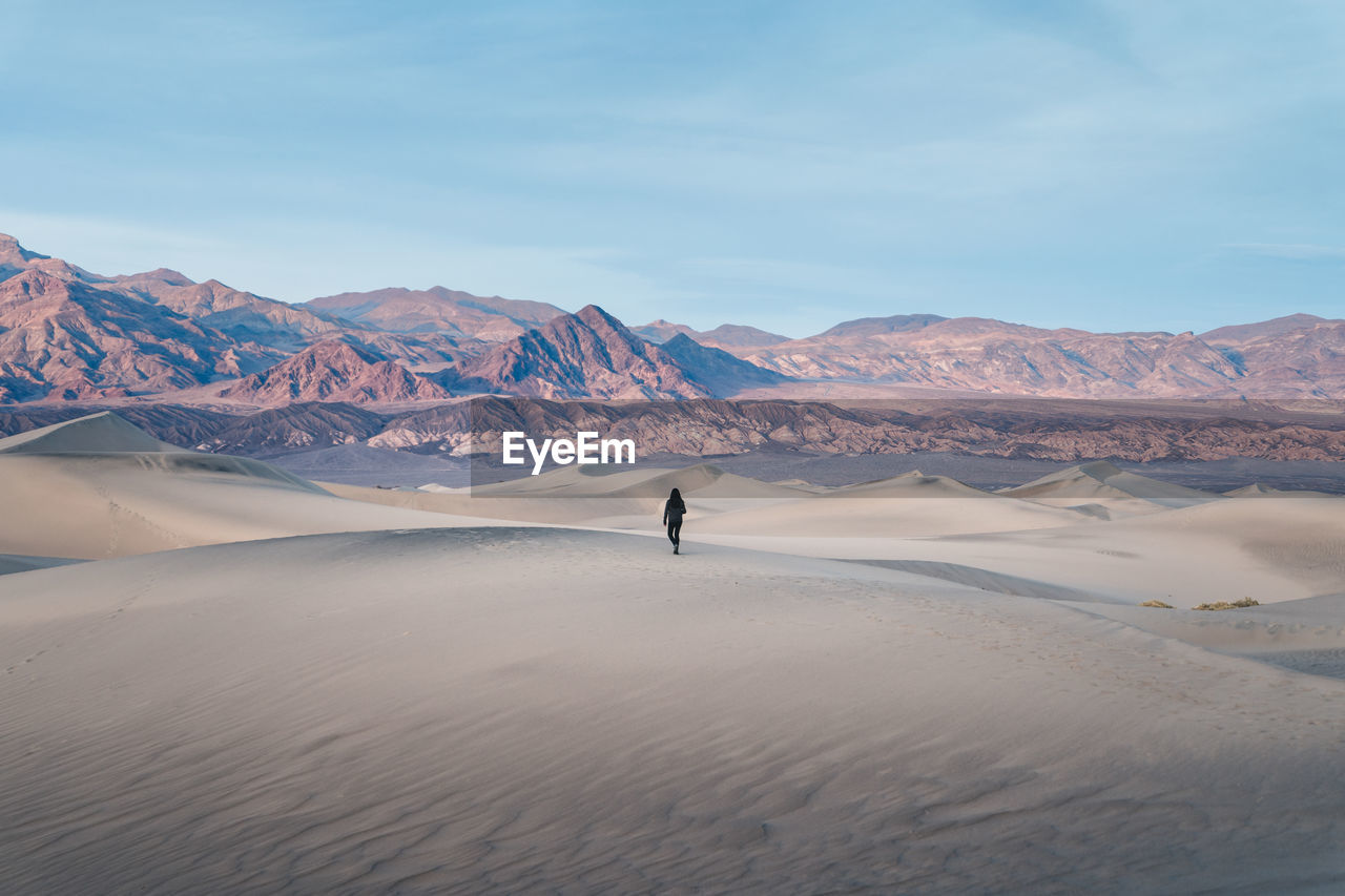 Woman walking on desert against sky