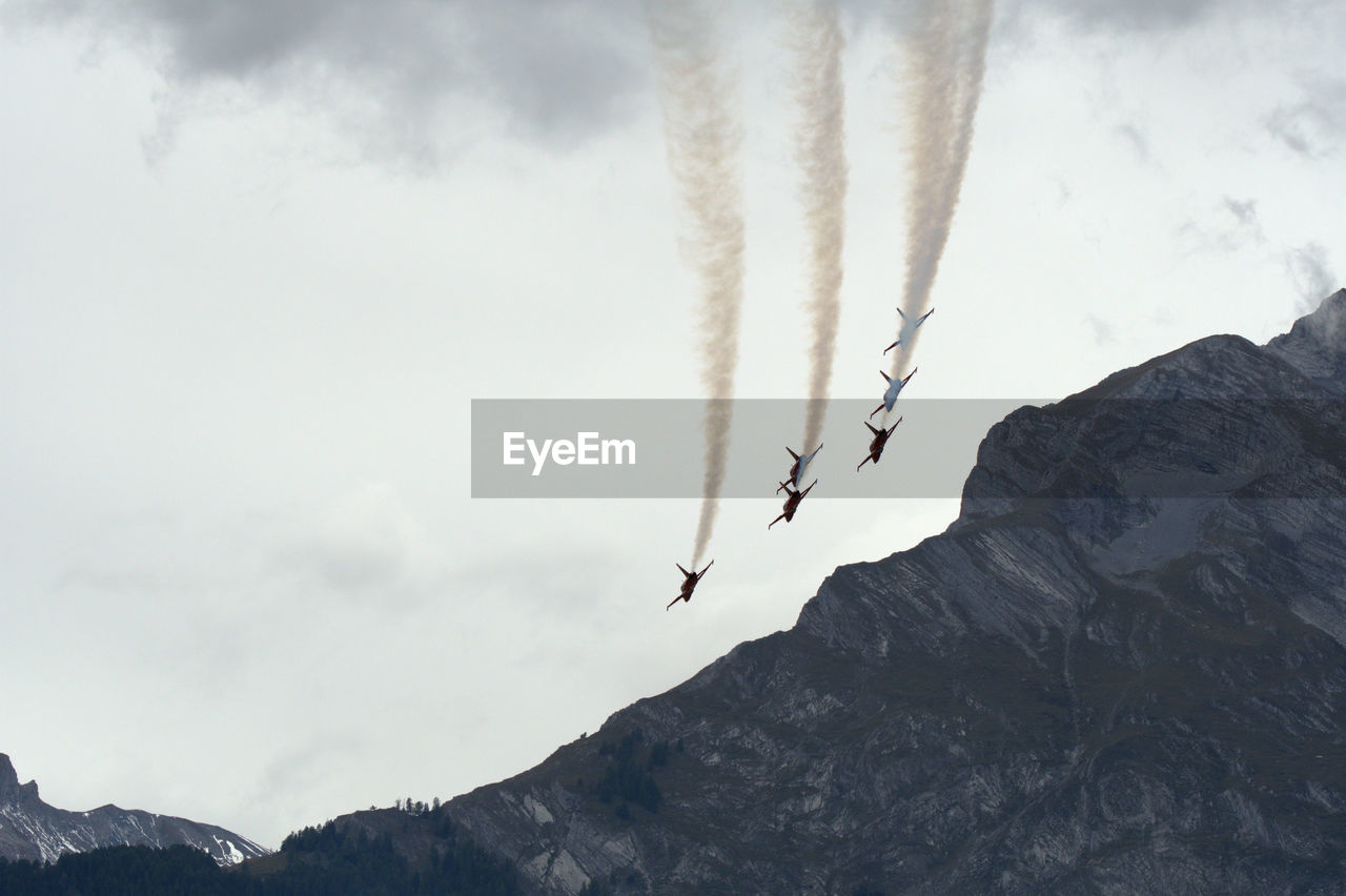 Low angle view of jet planes emitting vapor trail over mountains in sky