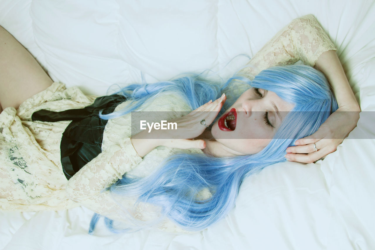 High angle view of woman with dyed hair yawning on bed