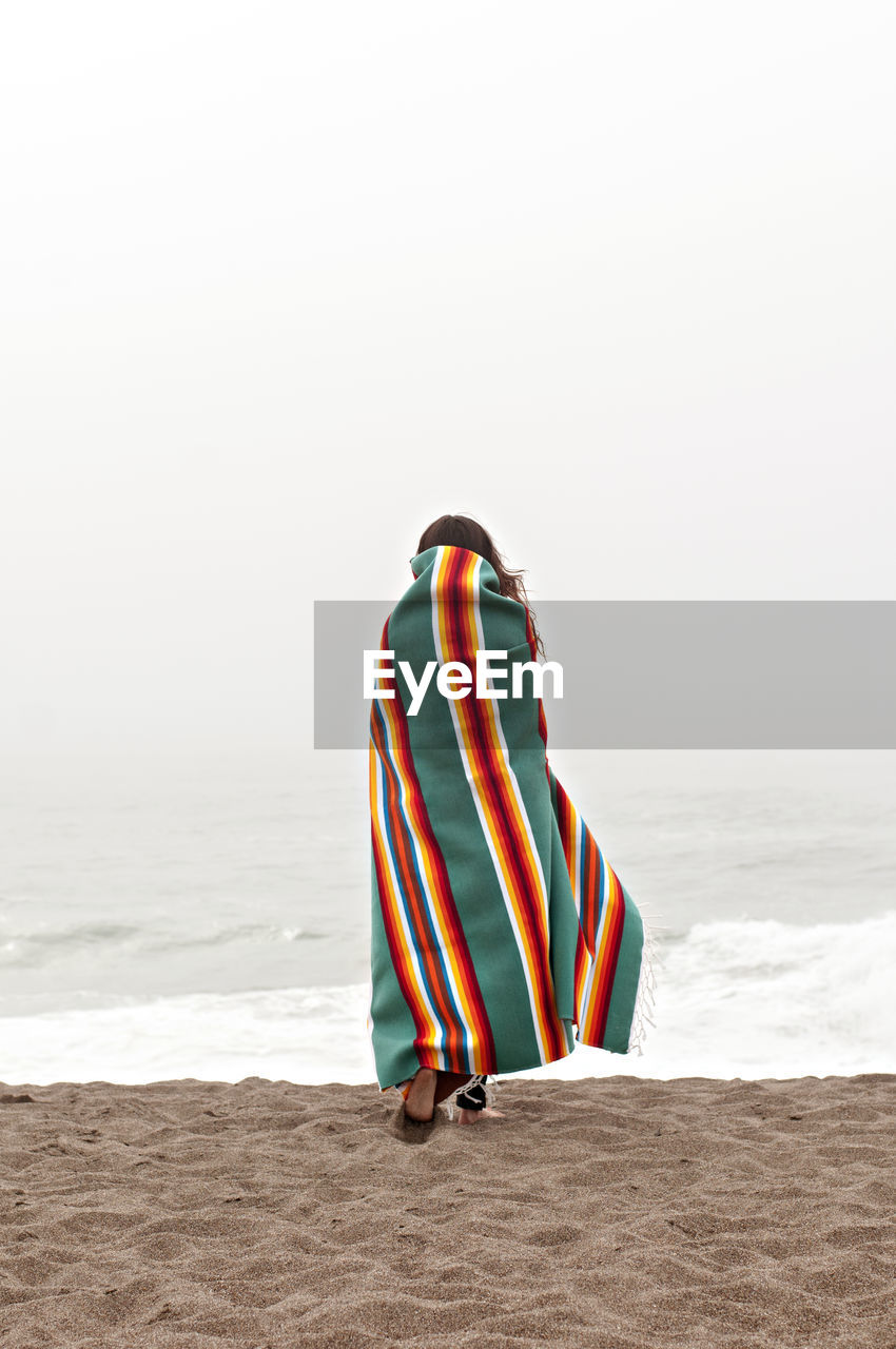 Rear view of woman wrapped in towel walking on shore at beach