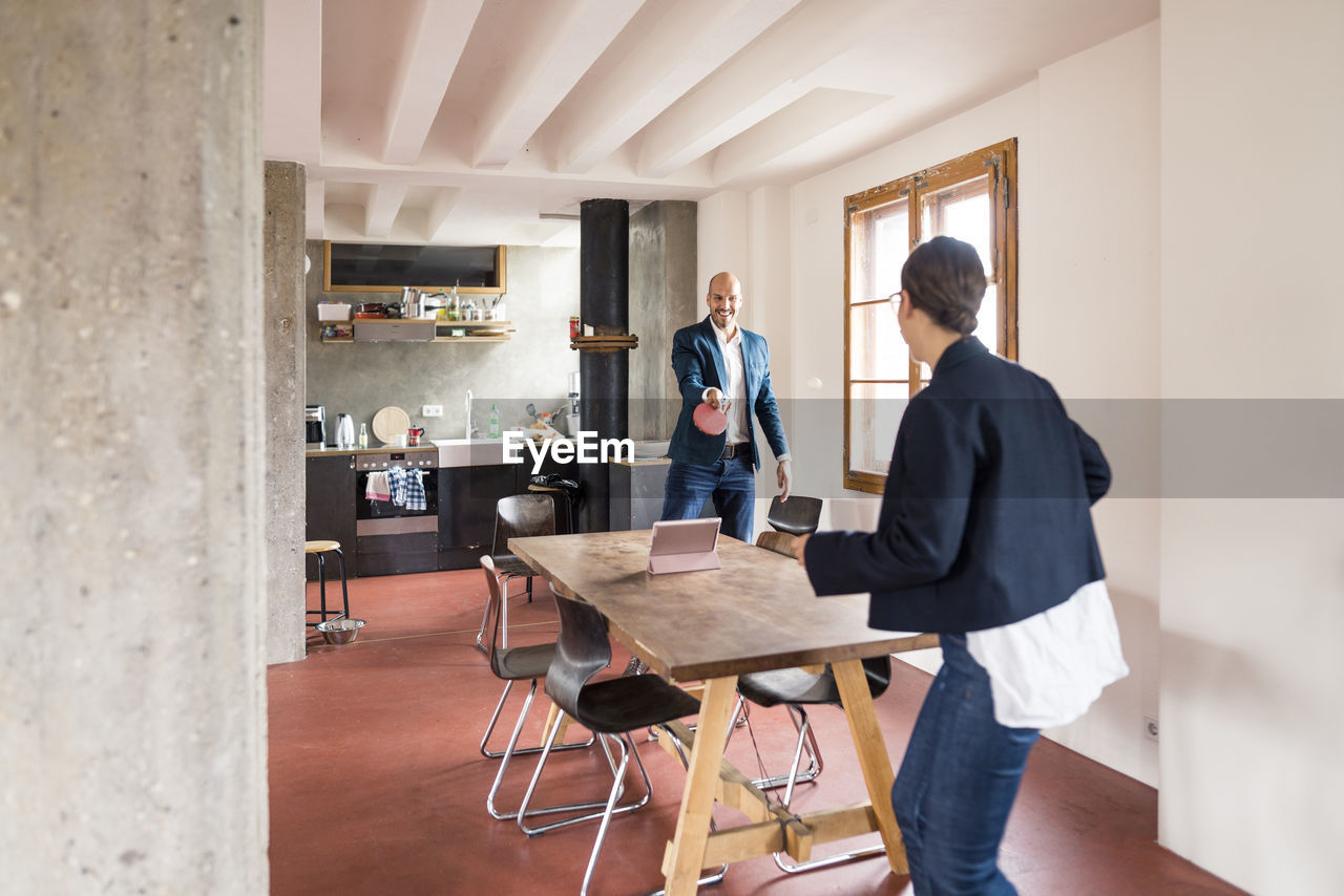 Carefree business people playing table tennis while standing at office