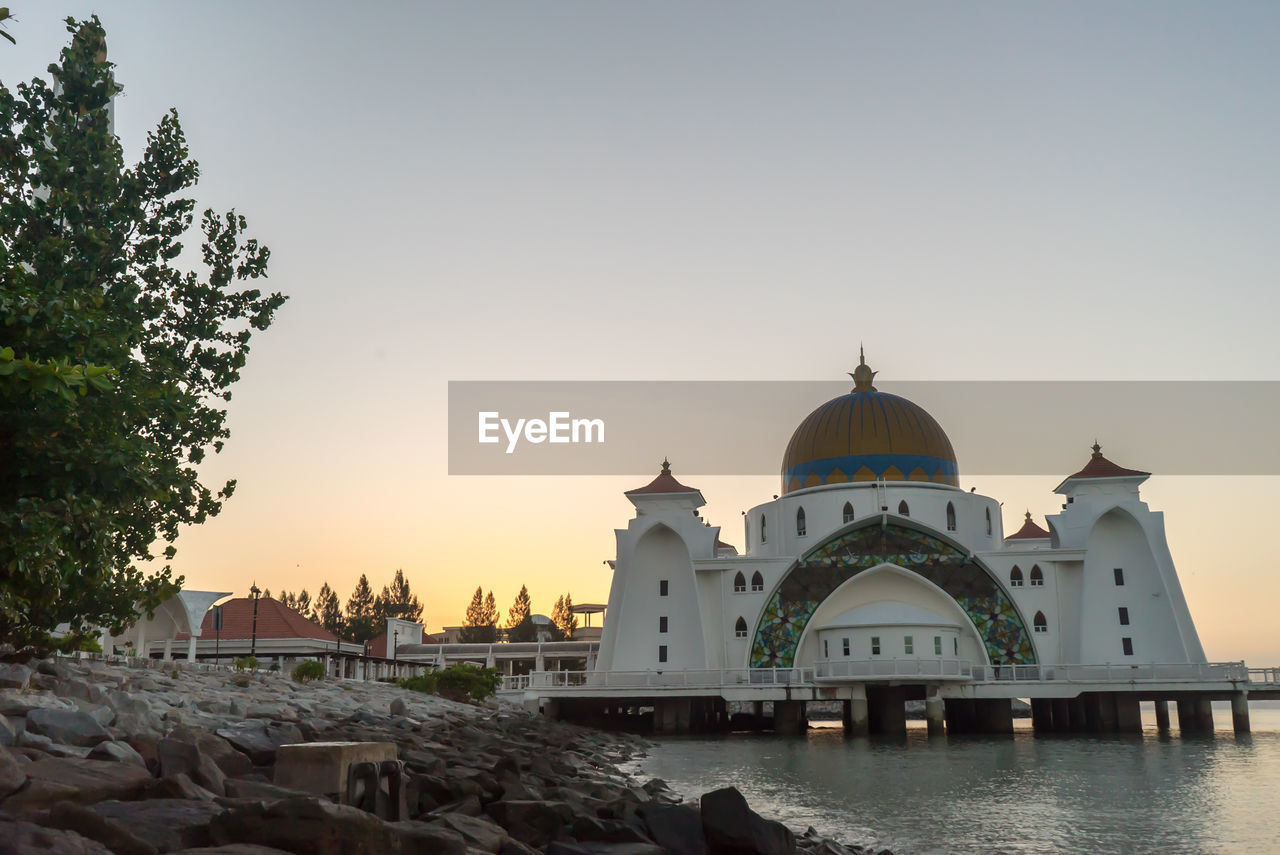 Mosque over sea against sky during sunset