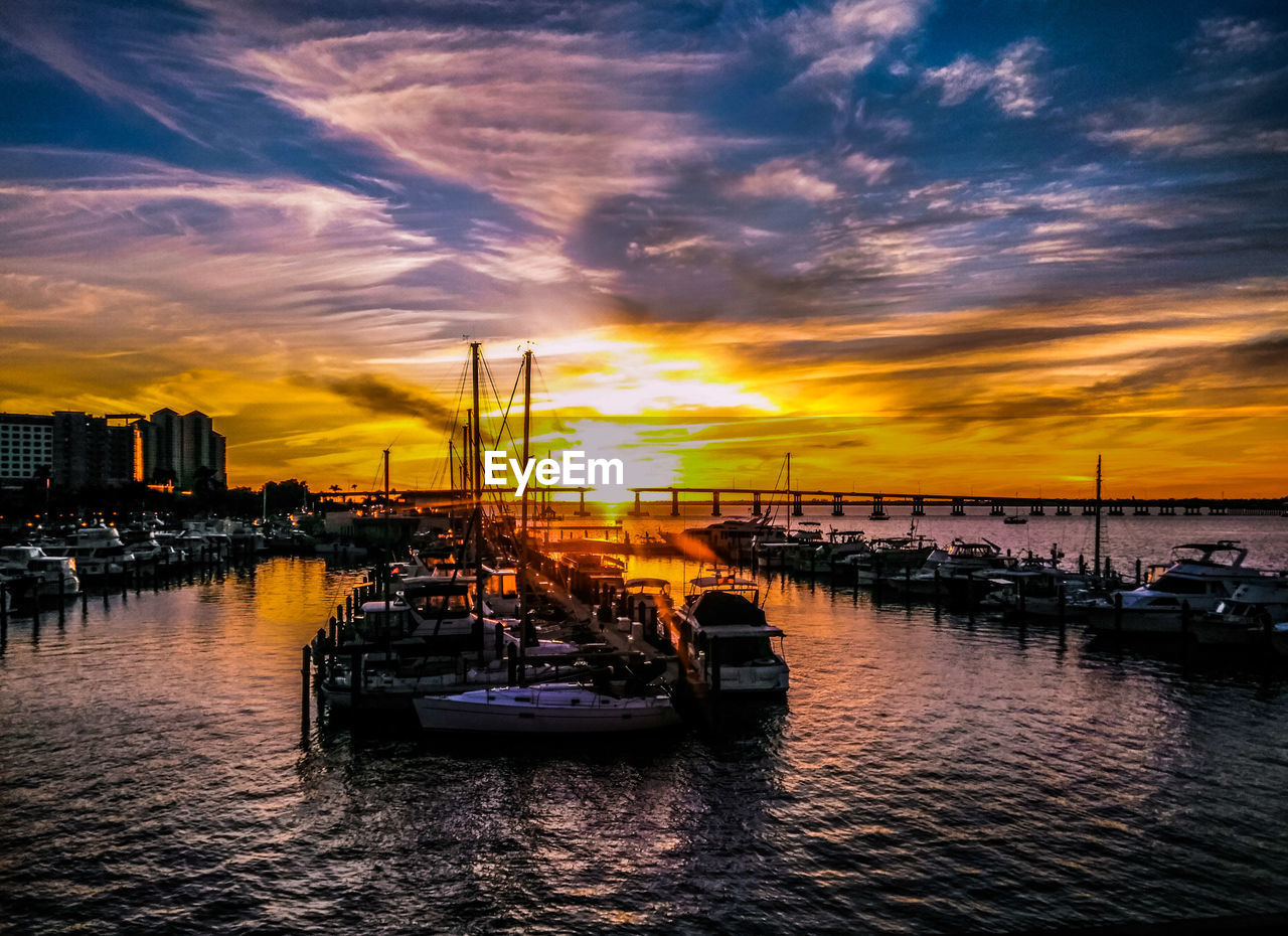 SAILBOATS MOORED ON HARBOR AGAINST SKY DURING SUNSET