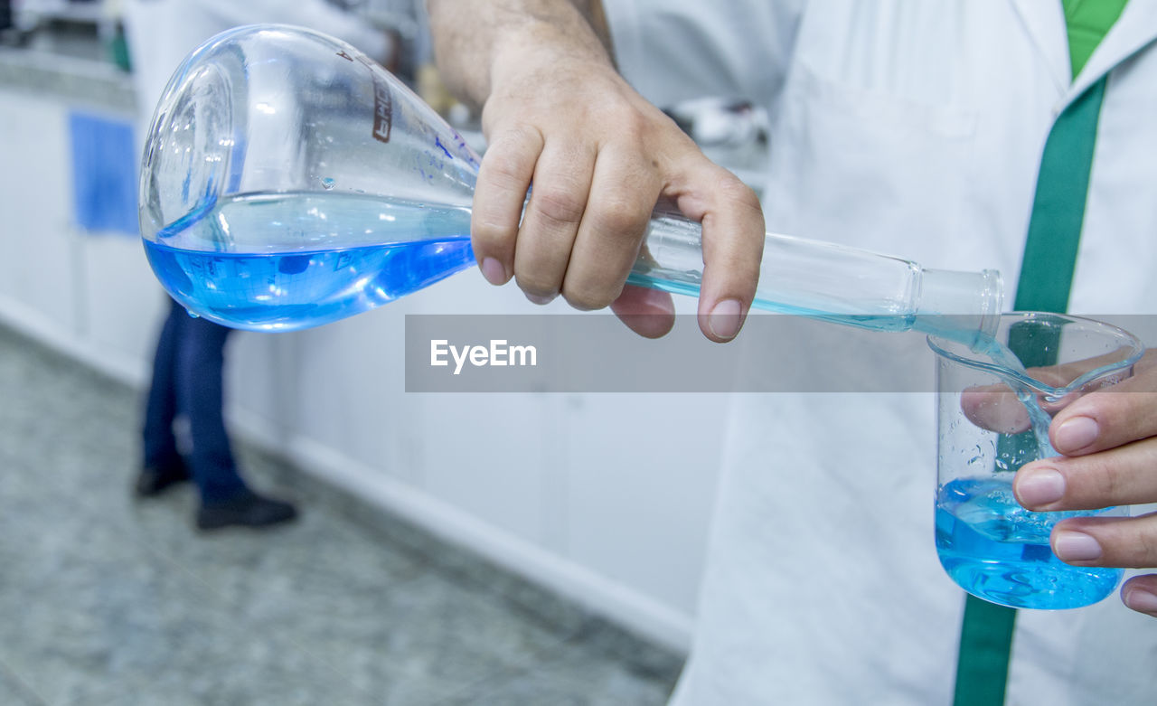 Midsection of scientist pouring liquid in beaker at laboratory