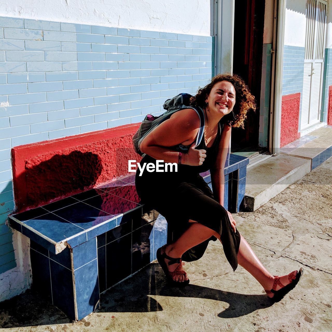 Full length of young woman sitting on bench smiling 