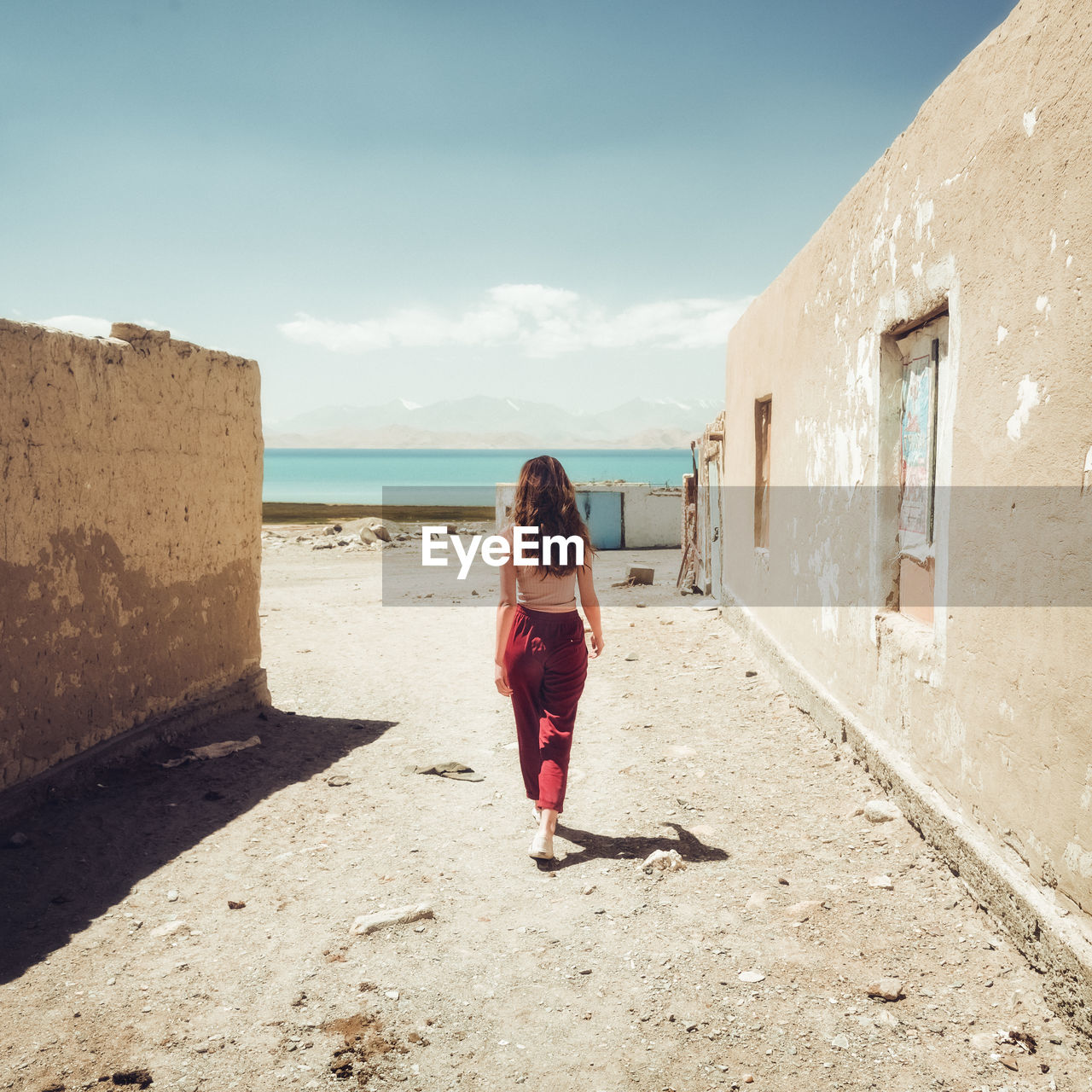 FULL LENGTH REAR VIEW OF WOMAN WALKING BY SEA AGAINST BUILDING