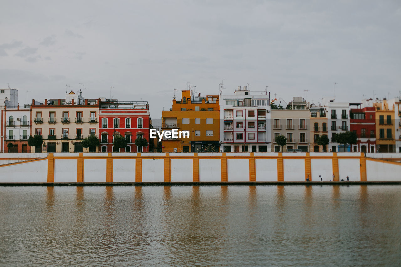 Residential buildings by river against sky