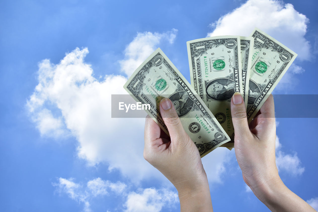 Close-up of person holding currency against blue sky