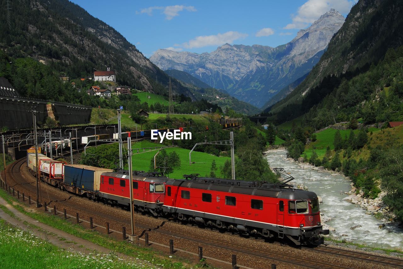 TRAIN ON RAILROAD TRACK AGAINST MOUNTAINS