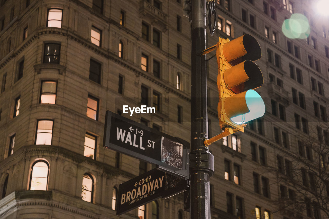 Low angle view of road sign against illuminated buildings in new york city.