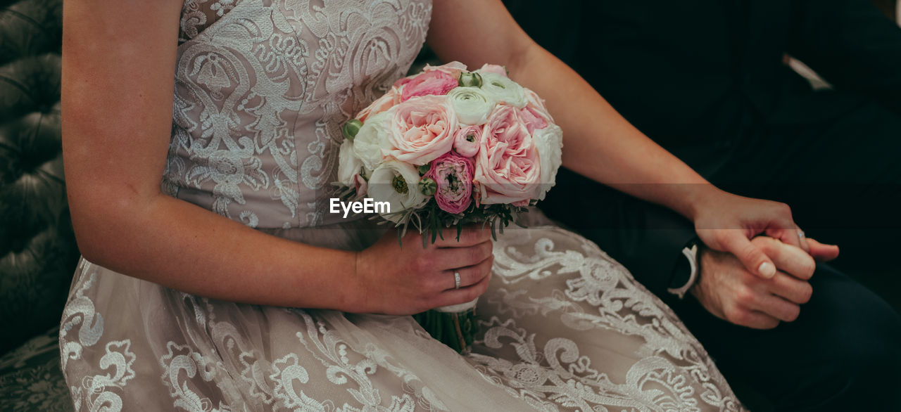Midsection of bride holding bouquet and groom hand