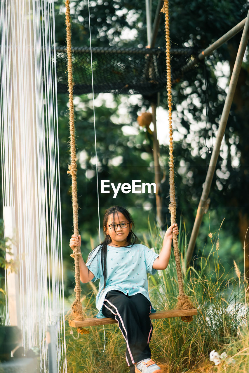 Portrait of smiling girl sitting on swing at playground