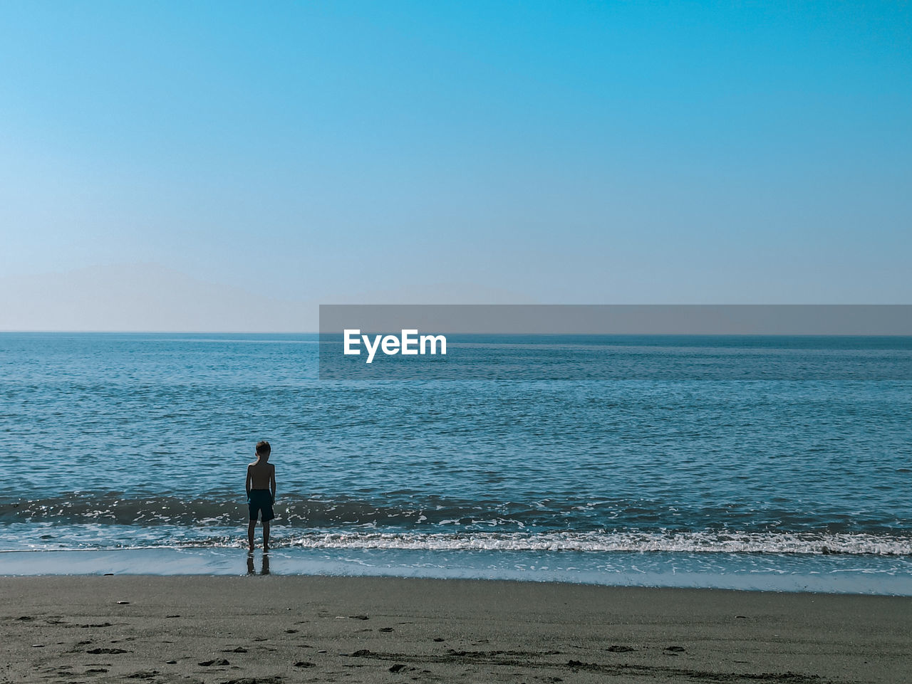 MAN STANDING ON BEACH AGAINST SKY AT SEA