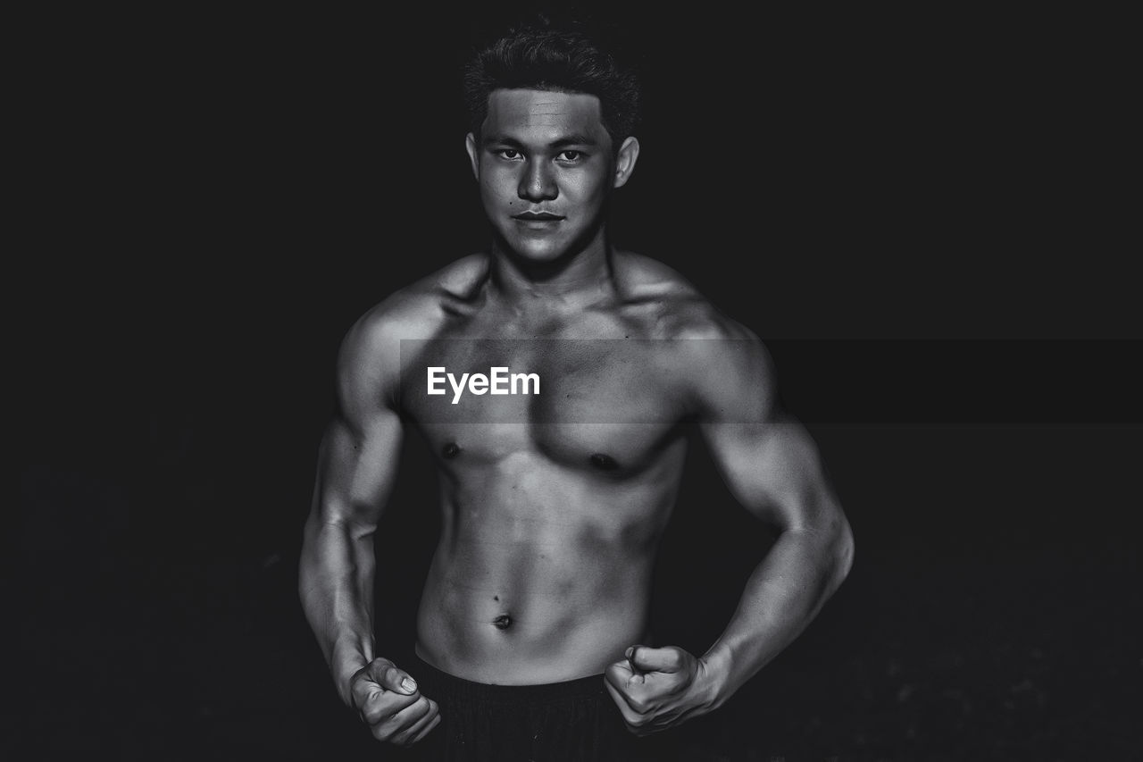 Portrait of confident bodybuilder showing build against black background