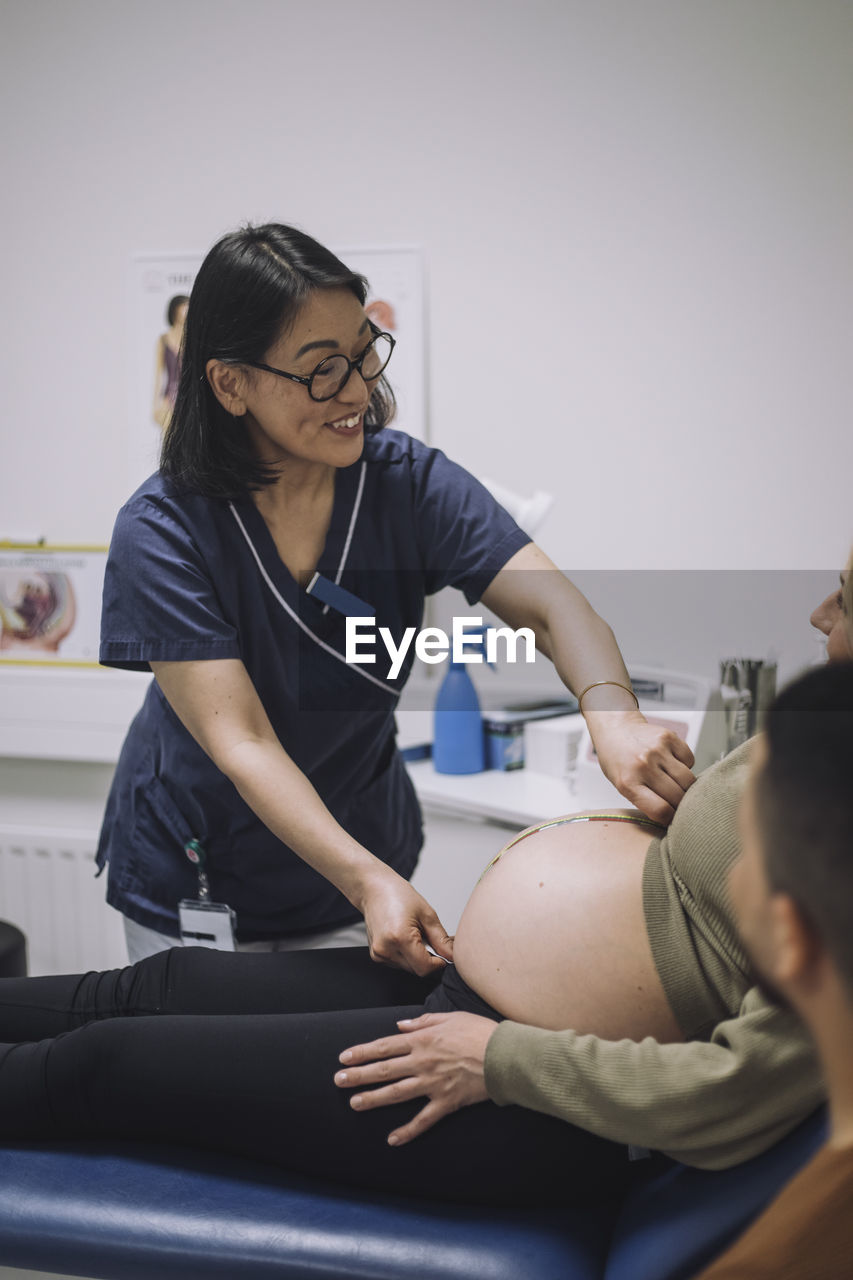 Smiling female doctor measuring abdomen of pregnant woman in medical clinic