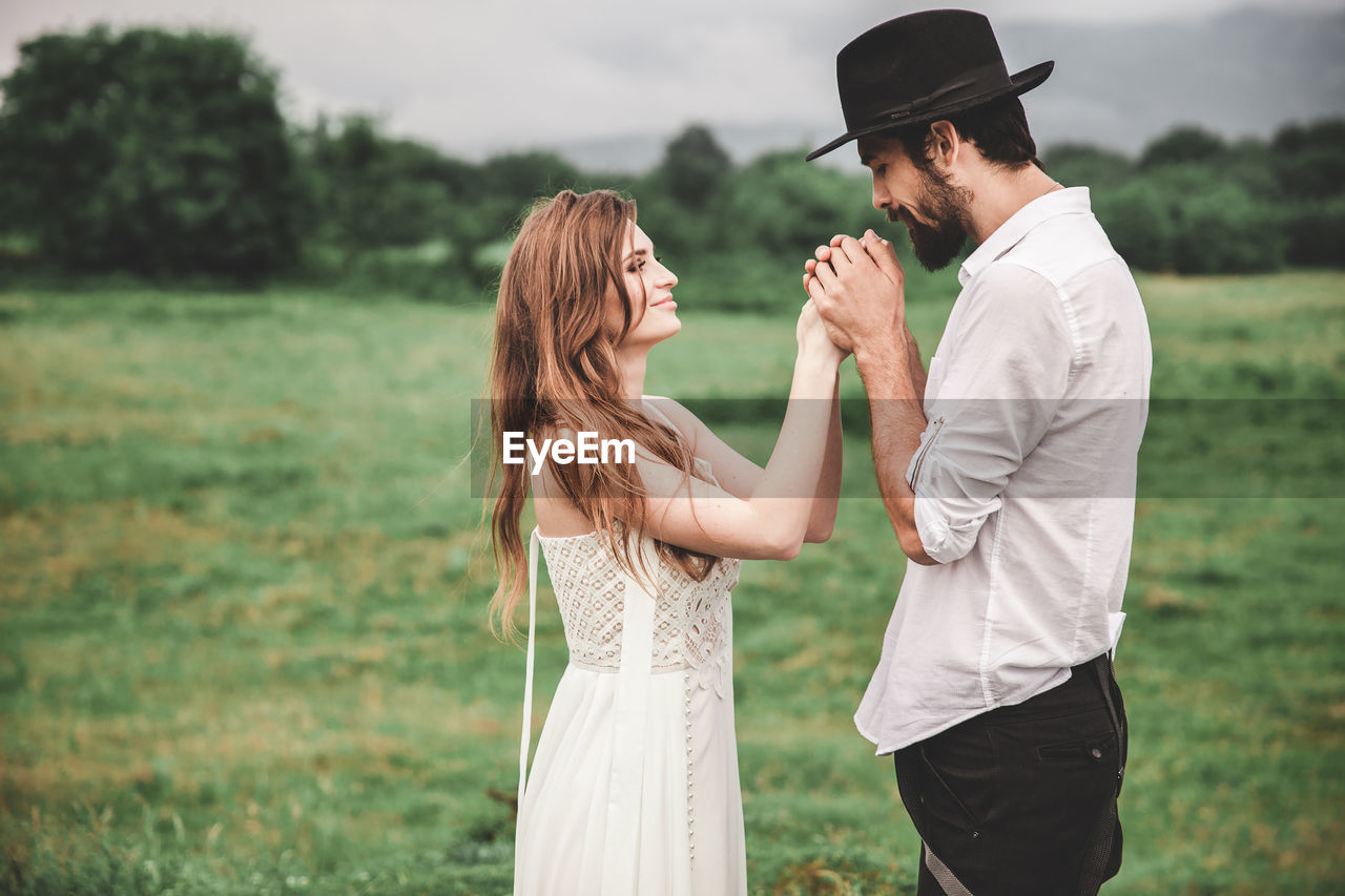 Side view of young couple holding hands while standing on field