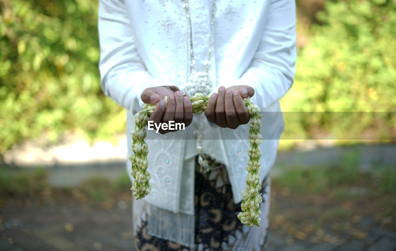Midsection of traditional groom standing in park holding jasmine necklace