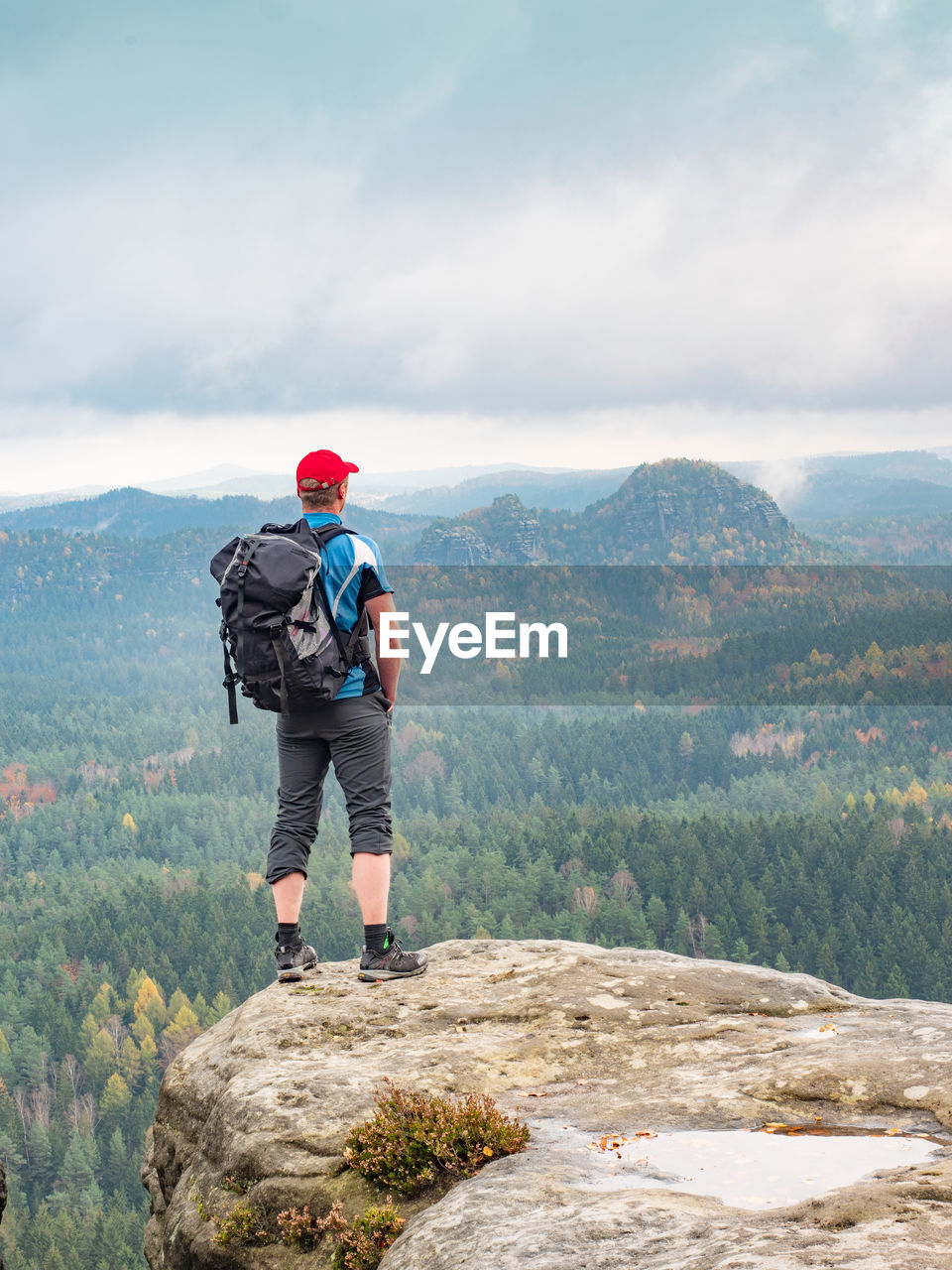 Sporty man hiker on the peak looking on mountain valley with sunbeams at colorful sunset in autumn