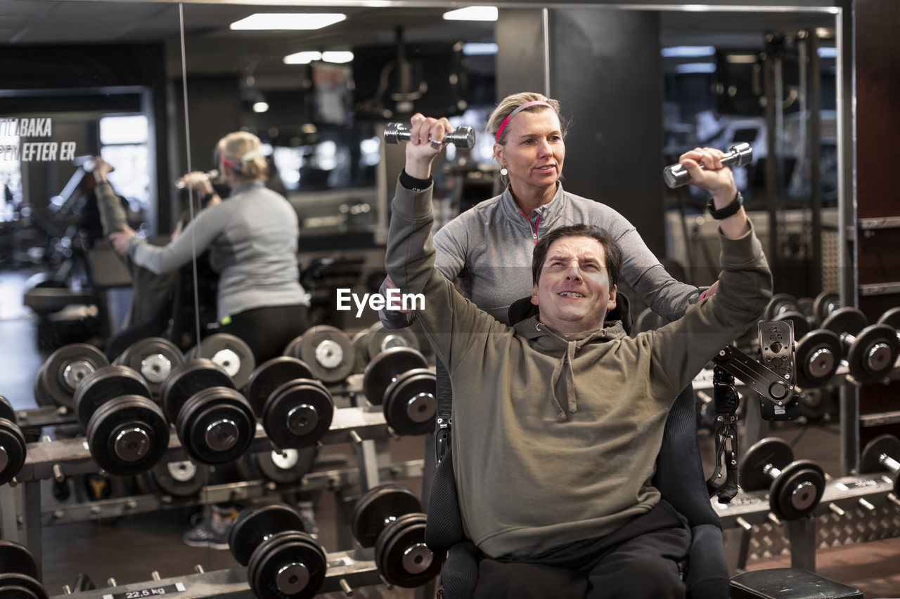 Man on wheelchair training in gym with personal trainer