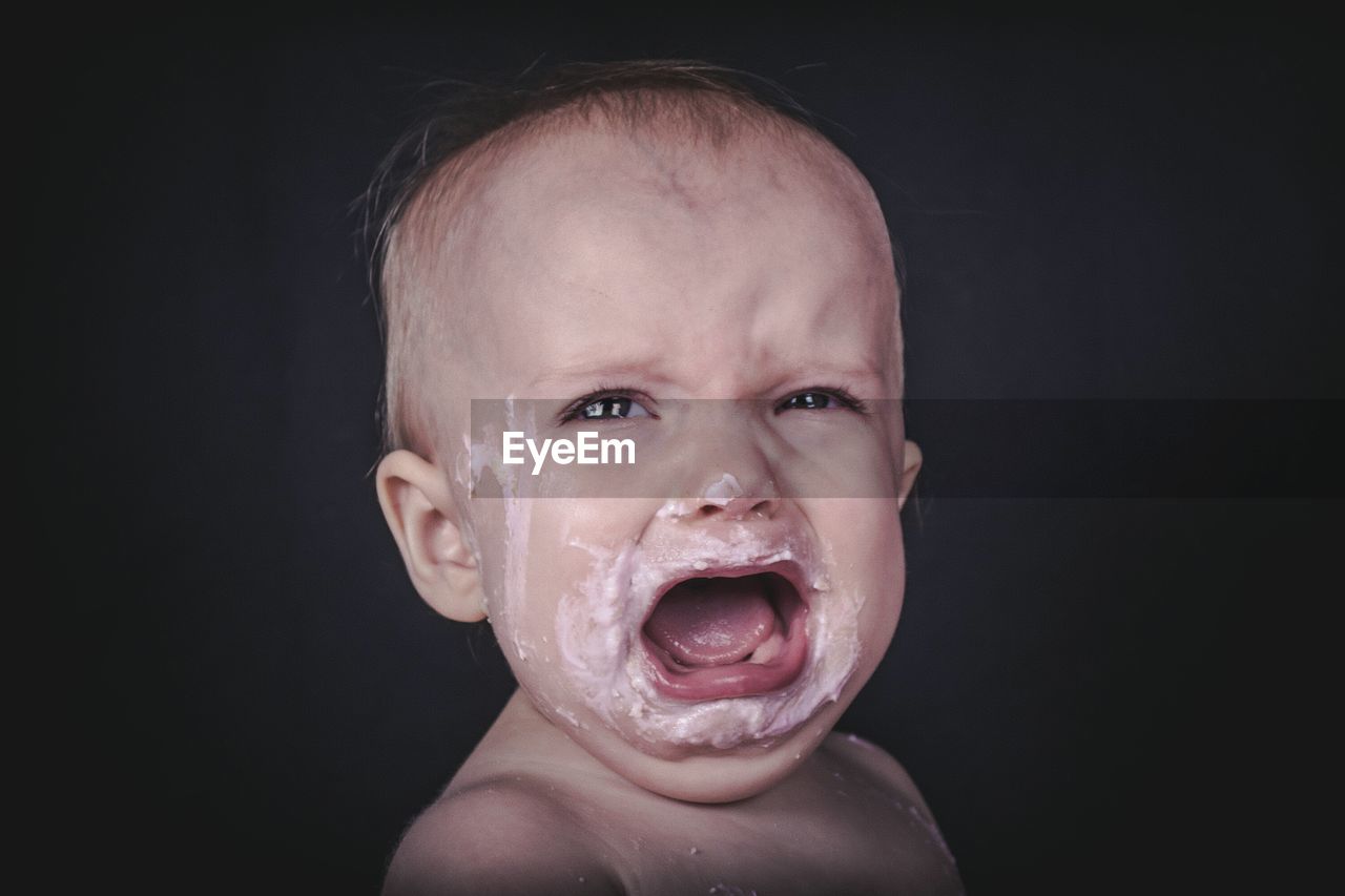 Close-up of baby girl crying against black background