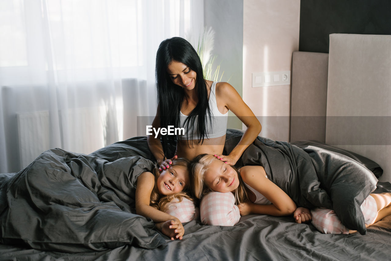 Happy young mom with two daughters resting on the bed